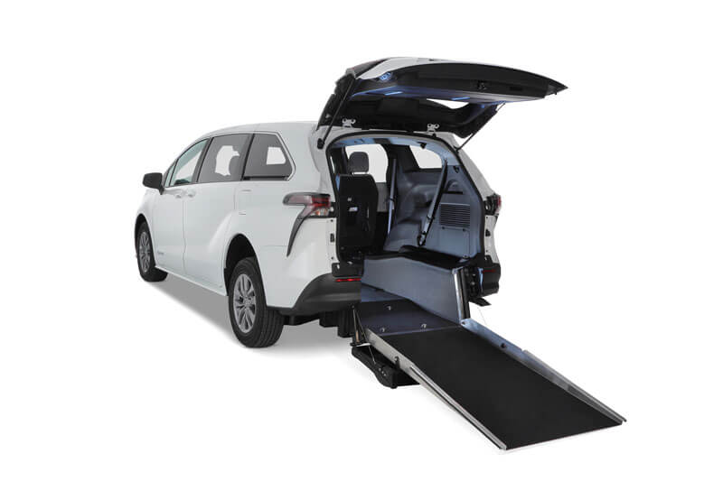 A white Toyota Sienna Hybrid minivan with its rear hatch open reveals a lowered ramp for convenient rear-entry wheelchair access.